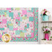 A shot of the lower right hand corner of the quilt, showing border fabric details. On the right hand side, a rustic wooden shelf holds pink and aqua watering cans that hold bouquets of matching flowers.