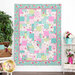 The completed Easy as ABC and 123 quilt in bright aqua, green, pink, and white, hung on a white paneled wall and staged with matching furniture such as watering cans with flowers and a loaded picnic basket.