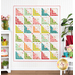 The completed Hearts At Home II Quilt in white and playful colors like lime green, orange, cherry red and pink, and teal blue. Hung on a white paneled wall, the quilt is staged with coordinating furniture and plants, flowers, and ceramic decor.
