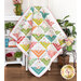 The completed Hearts At Home II Quilt in white and playful colors like lime green, orange, cherry red and pink, and teal blue, draped over a white ladder and staged with coordinating furniture and house wares.