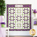 The completed Fruit of the Spirit Panel Star Quilt in white, purple, and green, hung on a white paneled wall and staged with coordinating purple and green housewares.