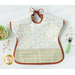 A top down shot of one side of the Toddler bib, showing a white fabric with multicolor polka dots and staged with a green bowl, fork, and cereal.