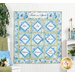 The completed Fruit of the Spirit Framed Panel Quilt in Ethereal, in shades of sky blue, cyan, leaf green, and white. The quilt is hung on a white paneled wall and staged with coordinating housewares, decor, and fabric from the collection.