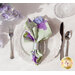 One of the Bloomerang napkins staged on a dining set. The pastel green side is largely visible with a little of the periwinkle lilac print peeking out. 