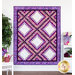 A shot of the full and completed Irish Chain quilt in bright purples, pinks, and white, hung on a white paneled wall and staged with coordinating furniture and decor.