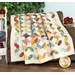 The Garden Path quilt colored in Gift of Grateful Praise, artfully draped over a brown loveseat, demonstrating flow and form, staged with matching flowers and decor.