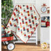 The completed Frolic quilt in cream, red, blue, pink, and yellow, artfully draped on a white quilt ladder and staged with coordinating  decor and furniture.