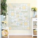 The completed Comfort of Psalms quilt in the Honeybloom collection, a palette of cream, light blue, and butter yellow in various floral prints. The quilt is hung on a white paneled wall and staged with coordinating furniture and decor.