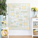 The completed Comfort of Psalms quilt in the Honeybloom collection, a palette of cream, light blue, and butter yellow in various floral prints. The quilt is hung on a white paneled wall and staged with coordinating furniture and decor.