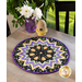 The completed Kaleidoscope Folded Star Table Topper in black, purple, and yellow, staged on a wooden table top with coordinating flowers and decor.