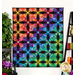 The completed Pineapple quilt in a rainbow of colors and prints, hung on a white paneled wall and staged with coordinating rainbow decor like fabric, jars, and flowers.