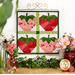 The completed June wall hanging, a pink, red, and green collage of four juicy strawberries, hung from a golden craft hanger on a white paneled wall with coordinating decor and flowers.