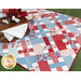 The Picnic quilt in action as a picnic blanket, staged with a brown picnic blanket that holds red flowers and an American flag.