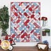 The completed Picnic quilt in red, white, and light blue, hung on a white paneled wall and staged with coordinating furniture and decor.