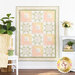 The completed Patchwork Sentiments quilt in white as well as pink, yellow, and green pastels, hung on a white paneled wall and staged with coordinating decor and furniture.