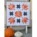 The completed mini quilt, hung outdoors on a white wooden quilt ladder and staged with pumpkins.