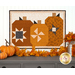 A quilted project featuring three stylized pumpkins in orange, cream, and black fabrics with geometric patterns, hung on a white paneled wall and stage with coordinating decor.