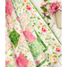 Close up photo of one edge of a finished pink, white, and green floral quilt showing fabric details with a basket full of flowers in the background.
