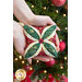 A model holds one of the ornaments in her open hands, with a blurred and decorated Christmas tree in the background.