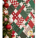 An angled close up on the criss cross design of the picnic quilt in red, green and cream, showing fabric and stitching details. Stitched holly leaves can be seen across the fabric.