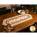 The Completed Up On The Housetop Table Runner, colored in cream and red, staged on a brown table with coordinating Up On The Housetop napkins and Christmas decor.