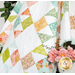 A shot of the draped quilt, showing fabric color, print, and piecing details, staged with coordinating pink flowers.
