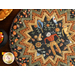 A top-down shot of the completed Point of View Folded Star Table Topper in warm fall colors from the Bittersweet Farm collection. The Topper is staged on a brown table with a jack-o'-lantern and small plastic cauldron filled with candy corn peeking in the shot from the left side.