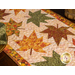 A top view of the table runner, demonstrating fabric and top quilting details. A wooden basket sits at the top right corner of the frame and an Autumn Celebration fabric napkin peeks into frame from the left side.