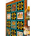 A side view of the Gather Together quilt in warm orange and teal colors with a shelf of coordinating fall decor on the right.