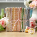 A stacked bundle of colorful fabric tied with a ribbon, surrounded by pink roses and spools of thread.