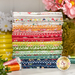 A stack of a colorful fabric bundle with floral patterns, spools of thread, and decorative flowers.