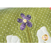 A super close up on the applique purple flower at the center of the pillow, demonstrating detail on the yellow button.
