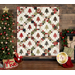 A winter themed cream quilt with evergreen trees and green, red, and brown fabric blocks making a lattice pattern, staged on a wood panel wall with a decorated Christmas tree.