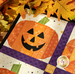 A close up shot of a grinning jack-o-lantern, surrounded by colorful yellow fall leaves with artful shadows and lighting cast across the project.