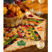 The completed table topper in autumn colors, staged on a dark wood table with coordinating napkins and fall decor, bringing attention to the applique leaves.