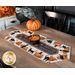 A table setting featuring the completed table runner with black cats and pumpkins and staged with coordinating decor and candy corn.