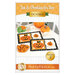 Front cover of the pattern featuring the two completed October mats in orange, black, and white, staged on a white table with coordinating decor with artfully frosted jack-o-lantern cookies.