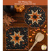 Two quilted hot pads, one round and one square, featuring a star design in orange and black displayed on a wooden table with coordinating seasonal decor. An orange banner at the top reads 