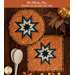 Two quilted hot pads, one round and one square, featuring a star design in cream and black displayed on a wooden table with coordinating seasonal decor. An orange banner at the top reads 