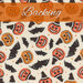 A swatch of cream fabric with tossed pumpkins wearing witch hats, bats, and sparkles. A bright orange banner reads 