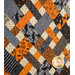 An angled close up on the criss cross design of the picnic quilt in black, gray, orange, and cream, showing fabric and stitching details. Stitched pumpkins can be seen across the fabric.