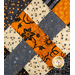 A super close up on the criss cross design of the picnic quilt in black, gray, orange, and cream, showing fabric and stitching details. Stitched pumpkins can be seen across the fabric.