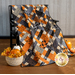 The picnic quilt, artfully draped over a black bench to show dimension and form. The quilt is surrounded by coordinating Halloween and fall decor.