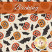 A swatch of cream fabric with tossed pumpkins wearing witch hats, bats, and sparkles. A burnt orange banner reads 