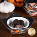 A vibrant fabric bowl cozy filled with dessert, surrounded by decorative Halloween items and a stack of three other matching bowl cozies.