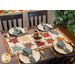 A wooden dining table set with four plates, silverware, and a colorful autumn-themed table runner in the center.