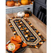 The completed table runner with pumpkins displayed on a wooden table and staged with coordinating decor