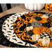 The four completed Oval Placemats colored in black, orange, and cream fabrics from the Hallow's Eve collection, slightly fanned out and staged on a wooden table.