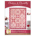 Front cover of the pattern showing the completed Chateau de Chantilly Patchwork Quilt in vibrant shades of red, pink, and white, hung on a white paneled wall and staged with coordinating furniture and decor.