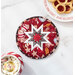 A top-down shot of the completed round hot pad in red, staged on a marble counter with coordinating decor like cookies for Santa and a mug of hot cocoa.